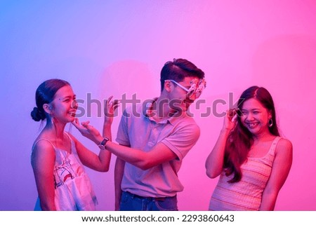 A funny playboy flirting simultaneously with two women. Hedonistic lifestyle lit with pink and blue neon colors.