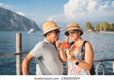 Funny and playful older couple eating ice cream cone. Portrait of husband slurping and wife biting a cold dessert in summer by a lake in Italy, Europe. - Powered by Shutterstock