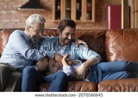 Funny playtime. Joyful elderly grandfather millennial dad tickle giggling tween kid boy on couch enjoy cute active game. Overjoyed three generation men family laugh aloud relax play have fun together Сток-фото © 