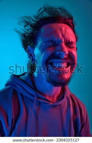 Funny portita of man posing with wind blowing into face against blue studio background in neon light. Concept of human emotions, facial expression, lifestyle. Meme look