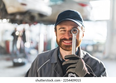 A funny portrait of an auto mechanic holding a metallic wrench close to his eye. High-quality photo