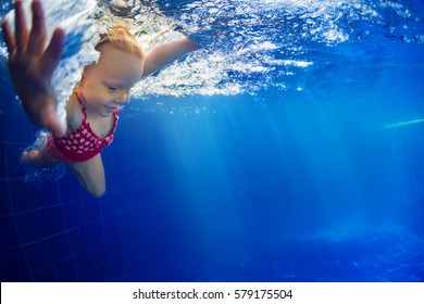 Funny portrait of baby girl swimming and diving in blue pool with fun - jump from poolside deep down underwater with splashes. Family lifestyle and summer children water sports activity with parents.
