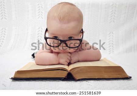 funny portrait of cute  baby in glasses lying over an old big book (vintage style)