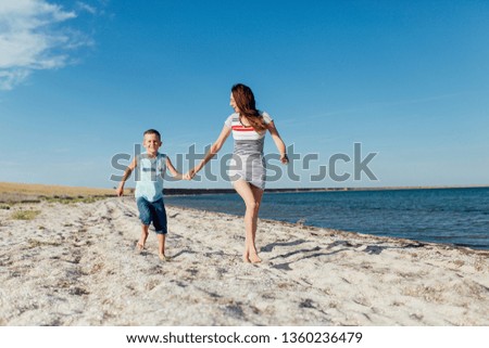 Funny portrait of a happy family on the beach. Mother is holding his son by the hand, they are running on the seashore and smiling.