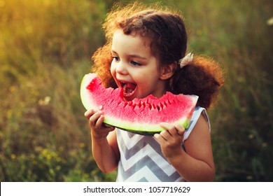 Funny Portrait Of An Incredibly Beautiful Red-haired Little Girl Eating Watermelon, Healthy Fruit Snack, Adorable Toddler Child With Curly Hair