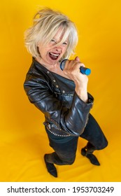 Funny Portrait Of Mature Woman. Beautiful Lady Have Fun As A Rock Star Dressed In Leather And A Walking Stick 
. Mature Woman On Colored Backgrounds