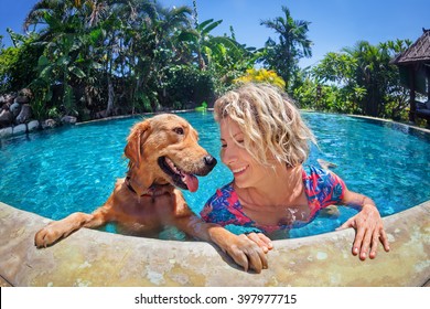 Funny portrait of smiley woman playing with fun and training golden retriever puppy in outdoor swimming pool. Popular dog like companion, outdoor activity and game with family pet on summer holiday.