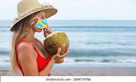 Funny Portrait Of Woman In Straw Hat Drinking Young Coconut On Tropical Sea Beach. New Rules To Wear Cloth Face Covering Mask At Public Places Due Coronavirus COVID 19. Family Holiday, Summer Travel