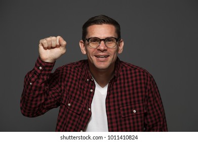 Funny Positive Man In Casual Clothes And Glasses Smiles And Knocks At Fictitious Door Or Window On Gray Background