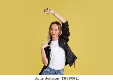 Funny Positive Naughty Young Woman Blonde In A Leather Jacket Posing On A Yellow Background. Place For Text. Shaka, Brah!