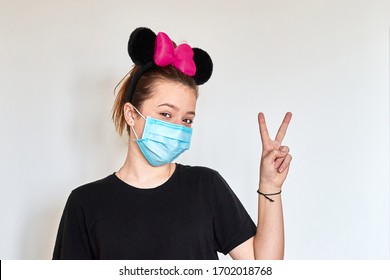 Funny Positive Teenage Girl In Hygienic Mask And Big Black Cartoon Mouse Ears Showing Victory Sign. Defeat Covid-19 Concept