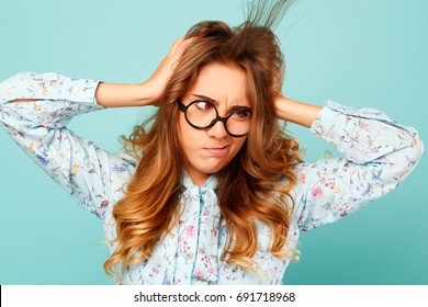 Funny pretty woman holding hands on her head and trying to blow away hairs from face over blue background