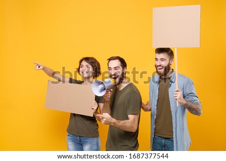 Funny protesting people guys girl hold protest signs broadsheet placard on stick scream in megaphone point aside isolated on yellow background. Protests strikes picket concept. Youth against city