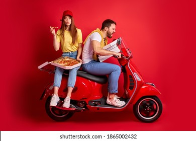 funny redhead woman rides with courier boyfriend delivering food orders on motorcycle, female is eating pizza sitting behind man, isolated red background