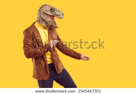 Funny reptile dancing on yellow studio background. Side view of happy man in leopard jacket and ugly dinosaur mask dancing isolated on yellow copy space background. Halloween party concept
