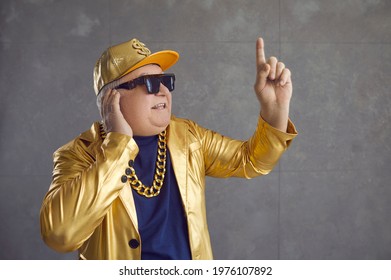 Funny Rich Senior Man In Golden Jacket Playing Music At Disco Party. Studio Shot Of Happy Old Grandpa In Baseball Cap And Bling Chain Necklace Enjoying Leisure Time And Mixing Songs On DJ Turntable