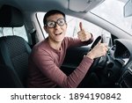 Funny and ridiculous idiotic nerd driver in big eyeglasses holding the steering wheel and smiling to the camera. Concept of a newbie driver distracted from the road