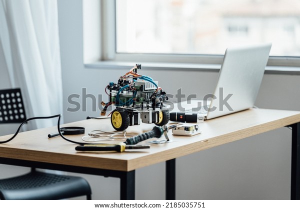 Funny robot standing at the\
table with laptop computer and different boards and\
microcontrollers. Programming, mathematics, science, technologies,\
DIY concept