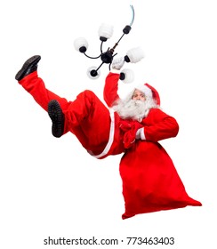 Funny Santa Claus Cling On Chandelier With A Bag Full Of X-mas Gifts. Falling Santa Carry Sack With Gift Box.