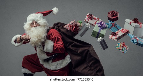 Funny Santa Claus running and delivering Christmas presents, he is checking time and losing gifts from his sack - Powered by Shutterstock