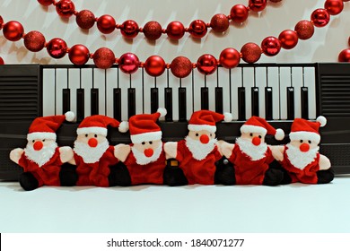 Funny Santa Claus Toys On Blurred Background Of Piano And Christmas Garland