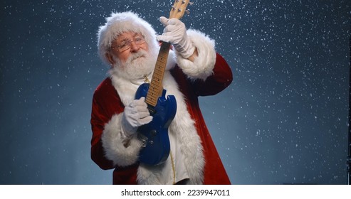 Funny santa clause is playing electric guitar and dancing while looking at camera, isolated over snowy blue background - christmas party, christmas spirit concept close up  - Powered by Shutterstock