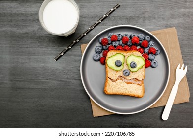Funny scary monster face smile on halloween sandwich toast bread with peanut butter, blueberry, raspberry on plate,bats on gray background close up. Kids child sweet dessert breakfast lunch food.