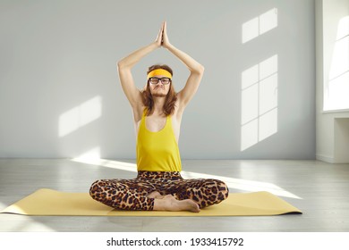 Funny Sceptic Suspicious Nerdy Man In Glasses, Yellow Headband, Tank Top And Leopard Leggings Doing Lotus Pose Yoga Exercise And Meditating With Discontent Displeased Disappointed Face Expression