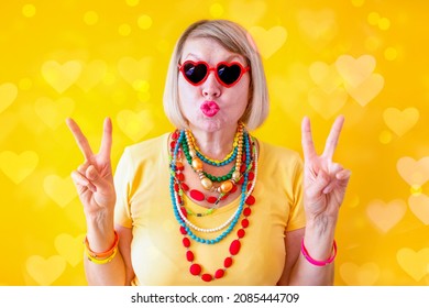 Funny senior woman in Valentine's Day funky action smile with glasses hearts on yellow background. Love and old people concept. Senior Citizen's Day.