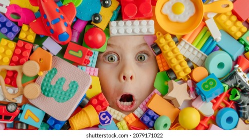 Funny shocked toddler girl among a lof her toys. Kid's face among od variety of toys. Horizontal panoramic banner. Top view, flat lay.