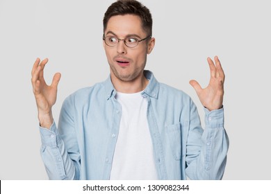 Funny shocked young man nerd looking at hands showing something huge, amazed confused guy in glasses bragging with large big size exaggerating gesture isolated on white grey blank studio background