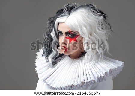 Funny shocking young woman in bright makeup and with a black and white hairstyle. Red star on the eye, rock and roll style mixed with glamorous style