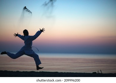 Funny silhouette of a woman jumping and throwing sand; sunset on the beach