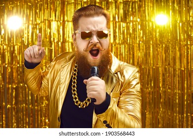 Funny singer in shiny golden jacket and gold chain holding microphone and singing songs at retro pop music concert. Happy bearded man performing at disco nightclub or enjoying time at karaoke party