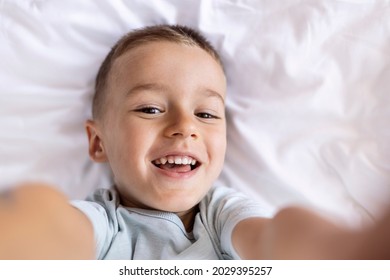 Funny Small Boy Taking Selfies And Grimacing. Smiling Cute Boy Taking Photos And Facetime Chatting. Portrait Of A Smiling Little Boy Holding Mobile Phone And Making Selfie