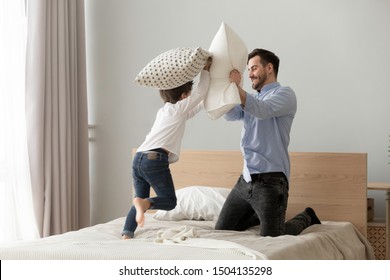 Funny Small Kid Son Playing Pillow Fight With Dad On Bed, Happy Cute Little Child Boy And Young Father Having Fun In Bedroom Enjoying Family Leisure Morning Lifestyle Activity Together At Home