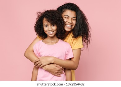 Funny smiling african american young woman and little kid girl sisters wearing casual t-shirts hugging looking camera isolated on pastel pink color background studio portrait. Family day concept