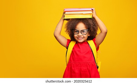 funny smiling Black child school girl with glasses hold books on her head. Yellow background - Shutterstock ID 2020325612