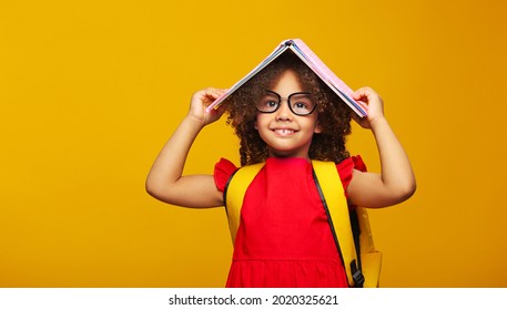 funny smiling Black child school girl with glasses hold books on her head. Yellow background - Shutterstock ID 2020325621