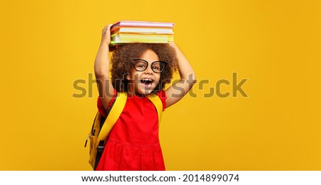 funny smiling Black child school girl with glasses hold books on her head. Yellow background