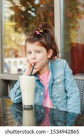 Funny Smiling Caucasian Preschool Girl Drinking Milk Shake With Paper Straw In Cafe. Child Kid Having Fun In Restaurant Patio Enjoying Food Drink. Happy Authentic Childhood Lifestyle. 