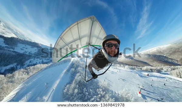Funny smiling hang glider\
pilot fly fast above winter ski resort. Creative shot of extreme\
sport