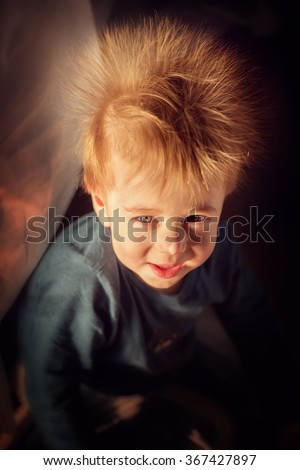 Funny smiling red haired little boy with electrified hair like big dandelion. Image with selective focus and toning