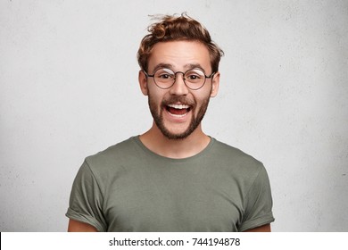 Funny Smiling Unshaven Male Wonk Wears Round Spectacles And Casual Clothes, Being Glad To Recieve Interesting Book As Present, Expresses Positive Emotions. People, Happiness, Positiveness Concept