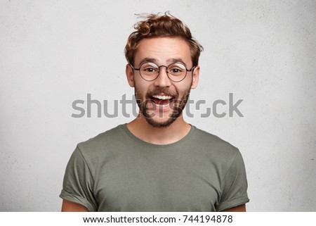 Funny smiling unshaven male wonk wears round spectacles and casual clothes, being glad to recieve interesting book as present, expresses positive emotions. People, happiness, positiveness concept