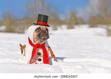 Funny Snowman Dog. French Bulldog Dressed Up With Christmas Costume With Red Scarf, Fake Stick Arms And Top Hat In Winter Snow Landscape