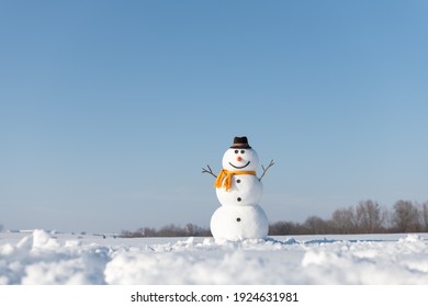 Funny snowman in stylish brown hat and yellow scalf on snowy field. Blue sky on background - Powered by Shutterstock