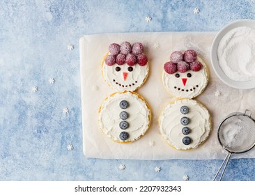 Funny snowmen made of pancakes, ricotta (cream cheese) spread, fresh berries and chocolate. Top view. Blue background. Christmas and new year breakfast concept. Festive winter dessert for kids.