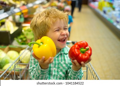 Funny spring shopping. Joyful beautiful child boy in supermarket buys vegetables. Pepper is yellow and red. Healthy food for children. Cute kid with smile