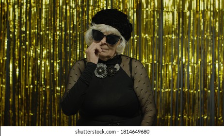 Funny Stupid Senior Old Woman Picking Nose With Silly Brainless Humorous Expression, Removing Boogers, Uncultured Habit, Bad Manners. Elderly Stylish Lady Grandma On Golden Background